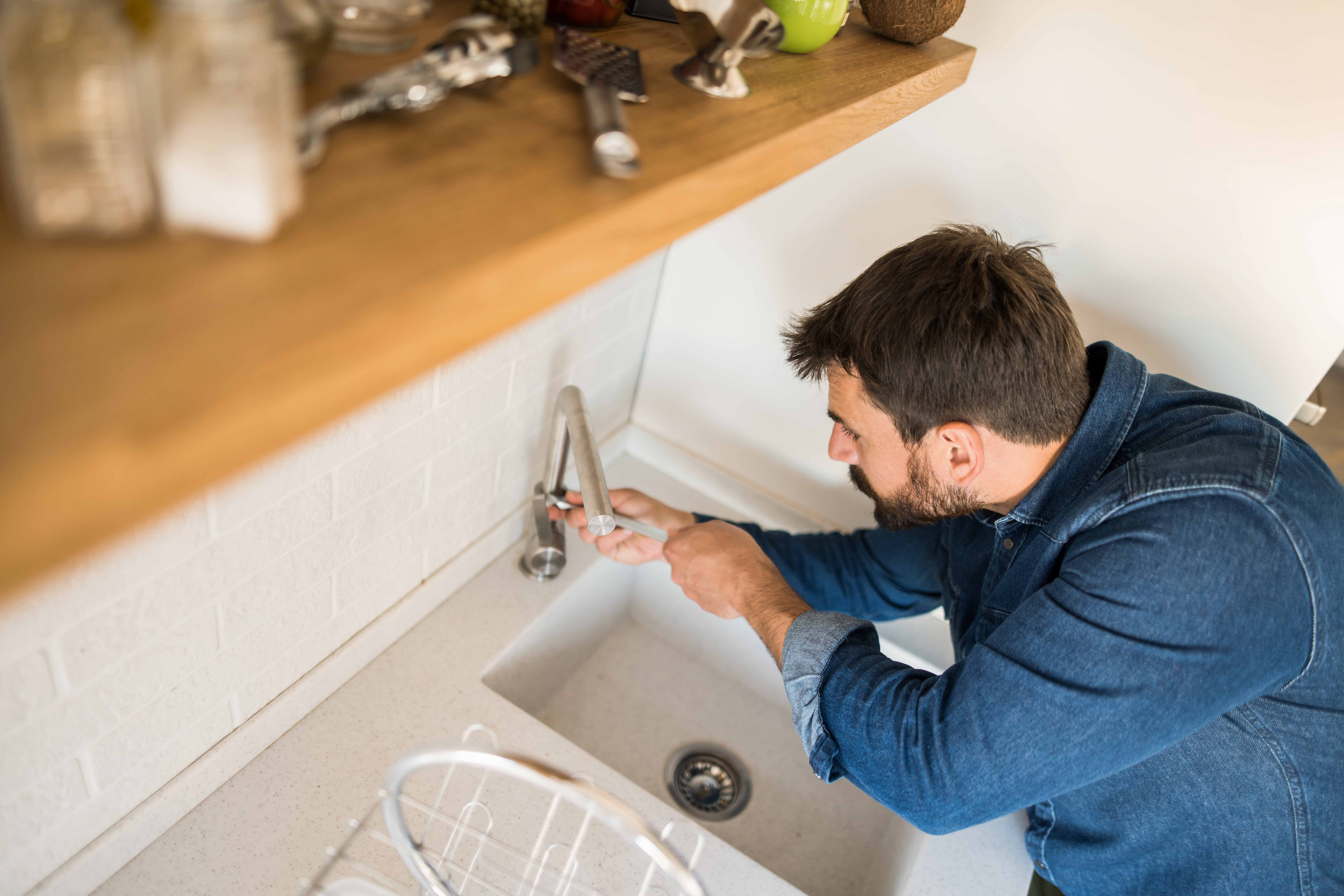 A man fixes a leaky dripping tap in his home.