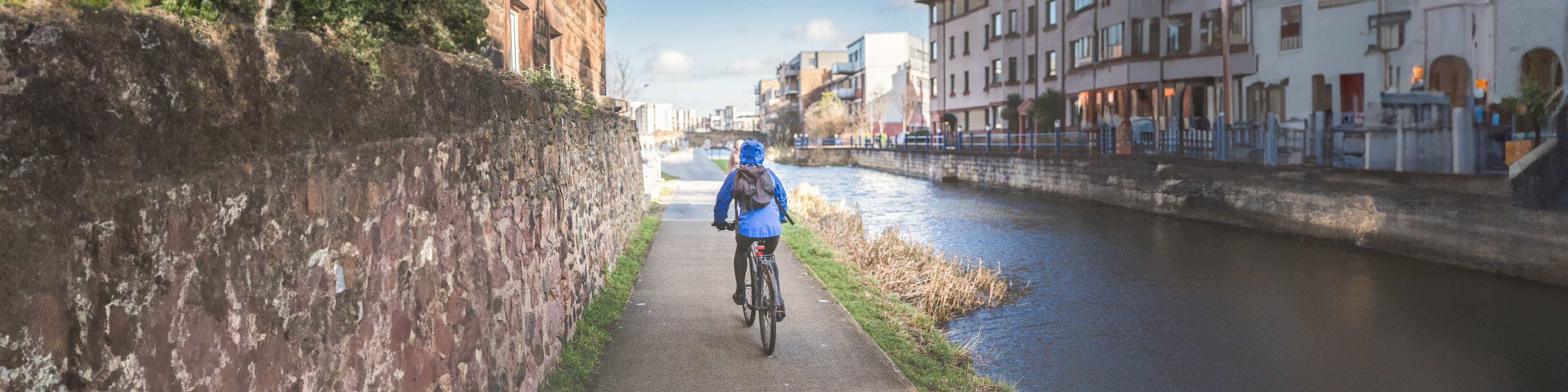 A person cycling a bicycle along a path next to a river