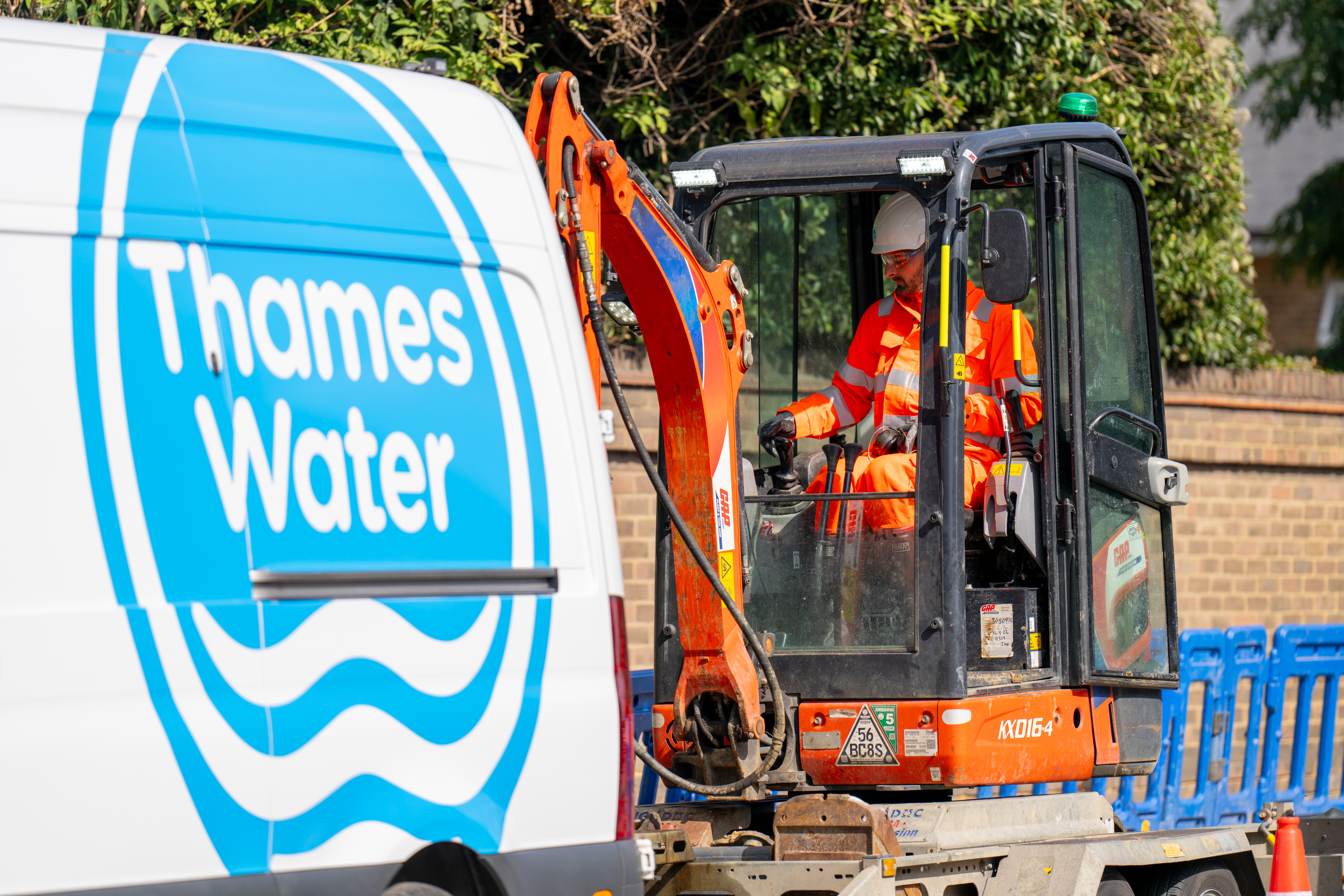A Thames Water worker operating a mini excavator with a van in the foreground