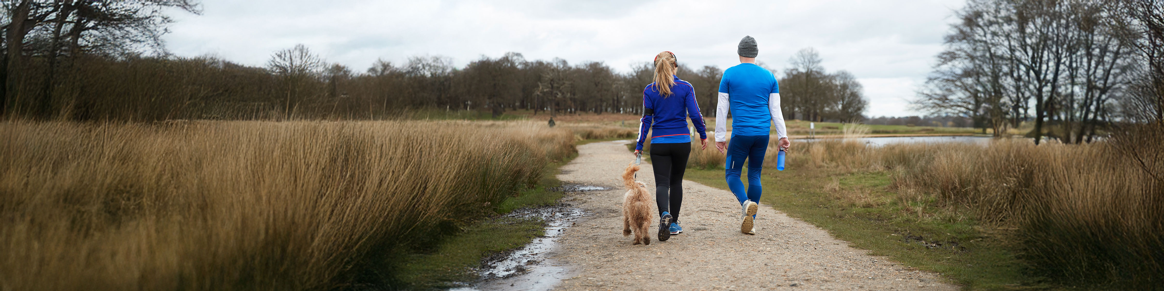 Two people walking a dog along a path near a lake
