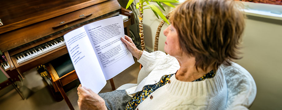 A woman sitting down reading a document next to a piano.