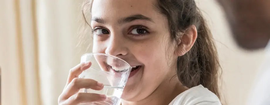 Young girl drinking water from a glass and smiling