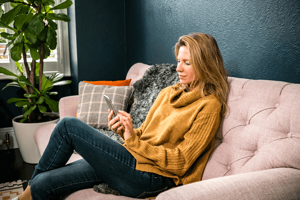 a customer sits on the sofa looking at something on their mobile