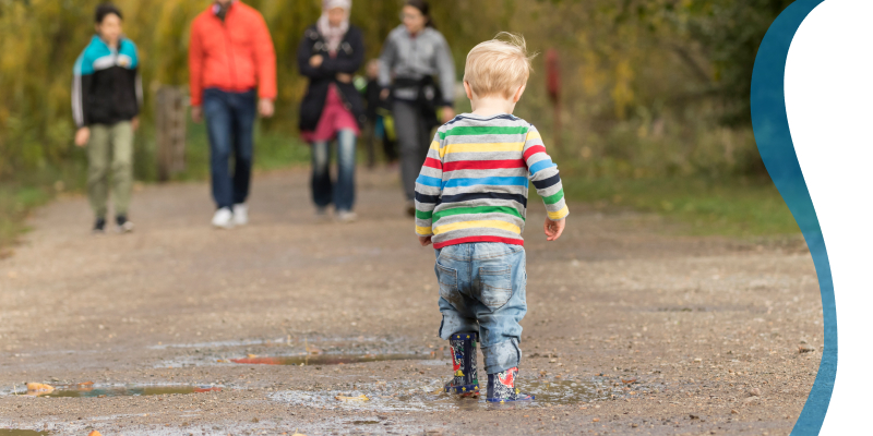 A young child splashing in a puddle with wellies on