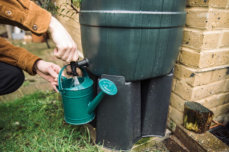 Person filling a watering can from a water butt.