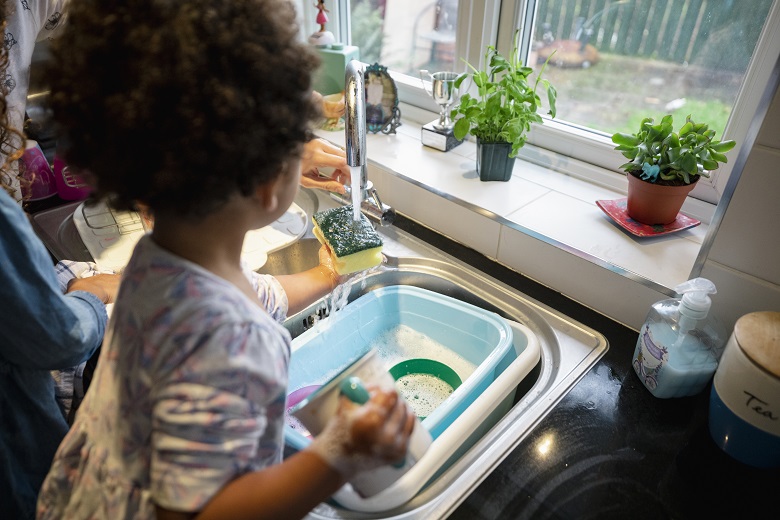 A young child cleaning a mug in a kitchen sink