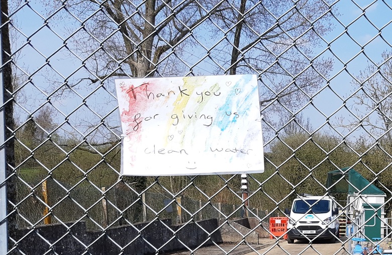 A handwritten message attached to a fence that reads 'Thank you for giving us clean water'.