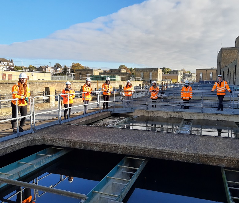 Eight Thames Water graduates dressed in orange PPE stand around a water tank