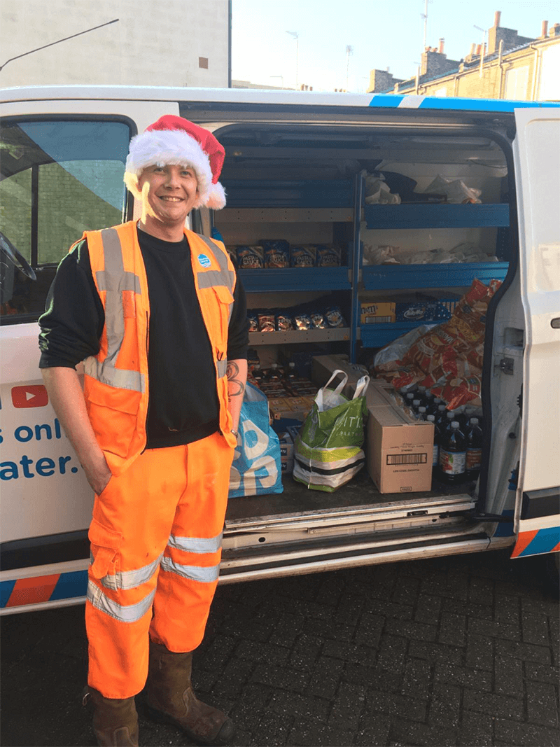 A man in orange hi-vis standing in front of an open van containing food donations