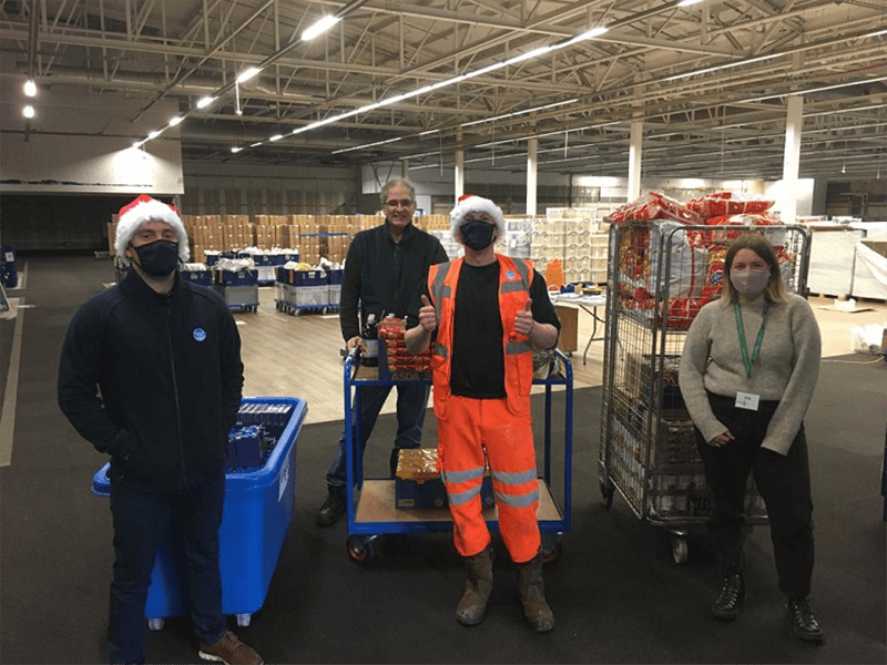 Four people in a warehouse with trollies containing food donations