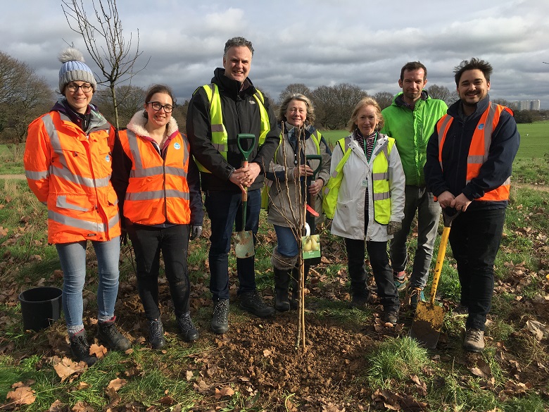 A group of volunteers standing behind a sapling