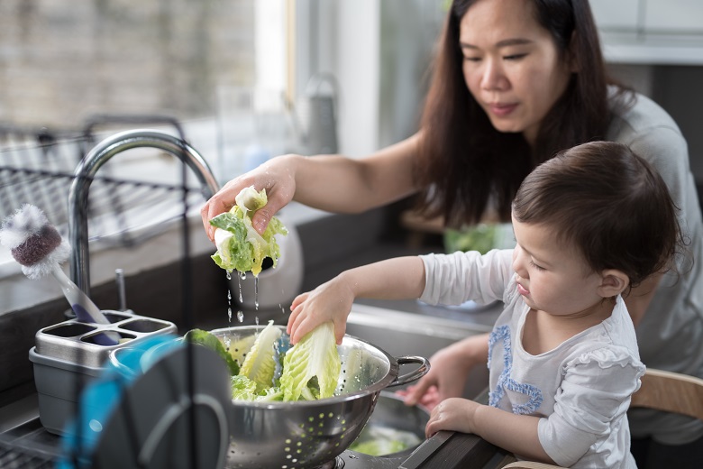 Mother with small child washing lettuce at the kitchen sink.