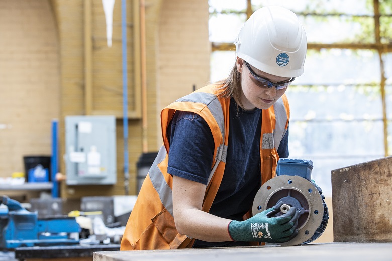 Woman in white hard hat examines motor