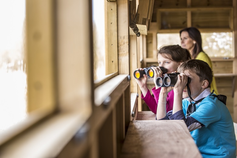Two children look through binoculars in a birdhide 