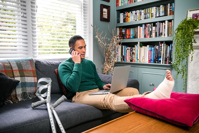 A man sits on a sofa with an injured foot resting on a coffee table