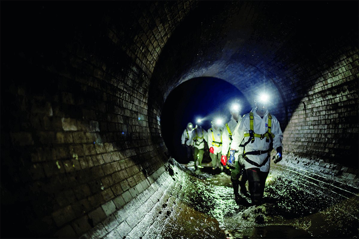 Engineers in PPE walk through a sewer