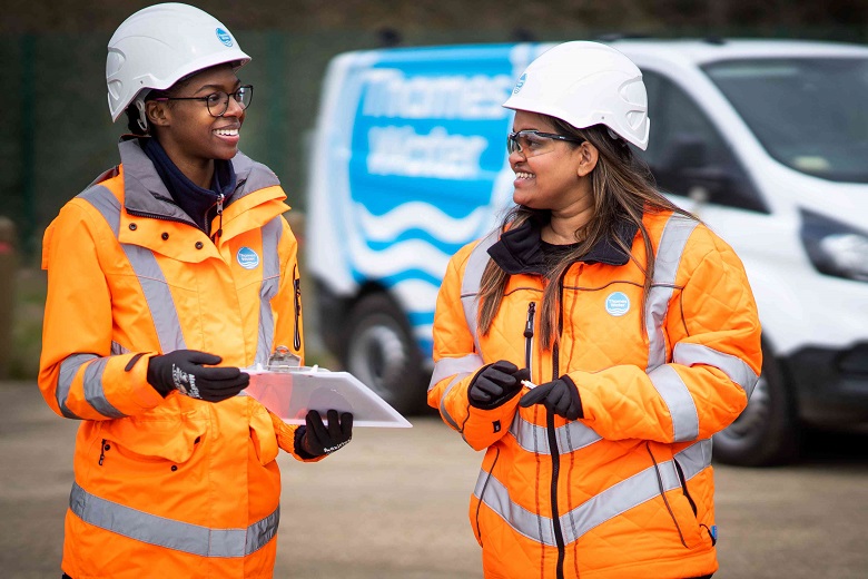Two women wearing orange hi-vis and white hard hats