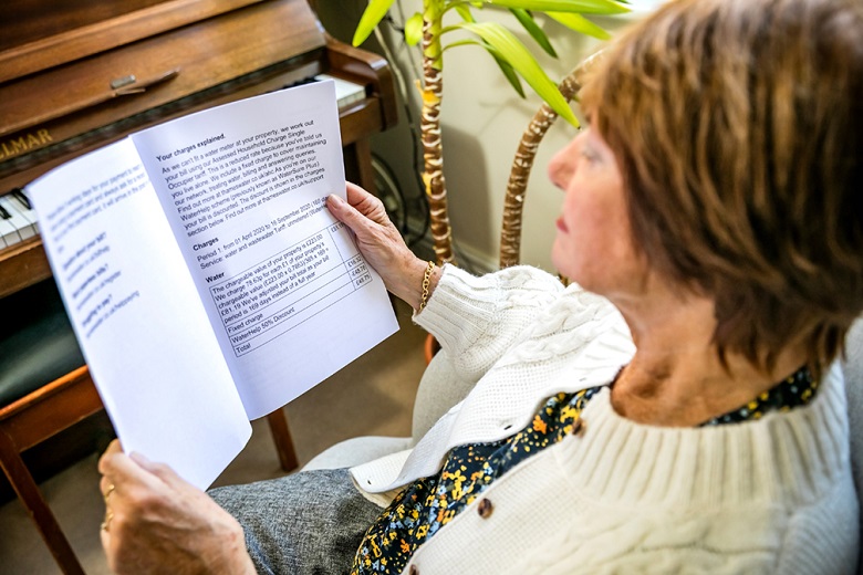 A woman in a white cardigan reads a large print bill