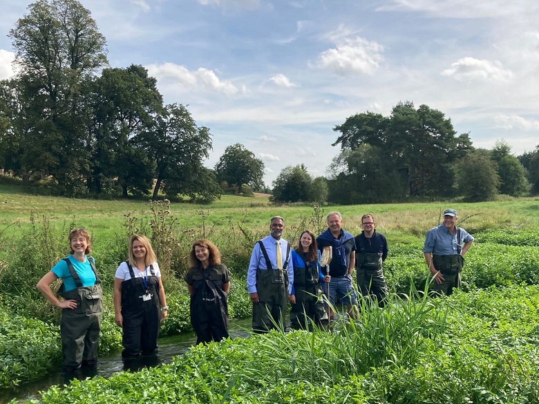 Eight people in green waders standing in a chalk stream