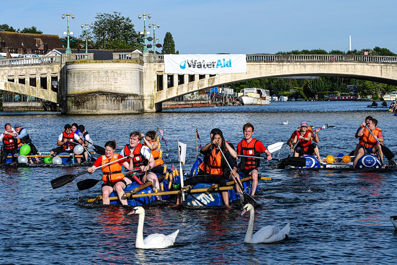 People wearing orange lifejackets paddling on rafts on the River Thames