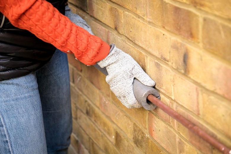 A woman in an orange jumper and gloves lags her outside pipes.