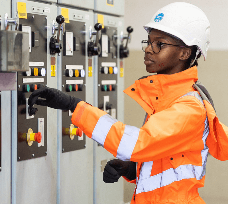 A woman in an orange high-vis inspects a control panel.