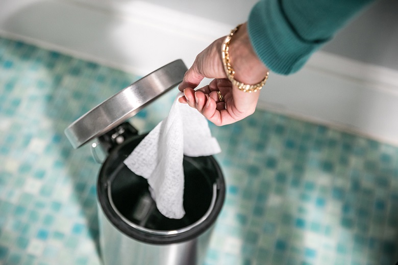 A person wearing a green top throws a wet wipe in the bin
