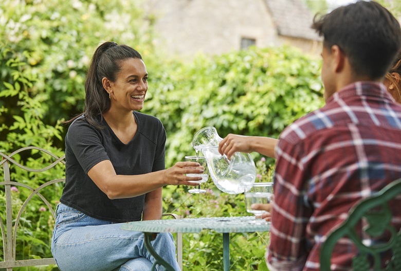 A women in a black top and blue jeans is poured a glass of water.