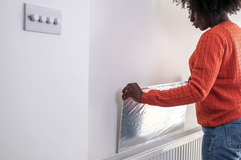 A lady in an orange jumper puts reflective material behind her radiator