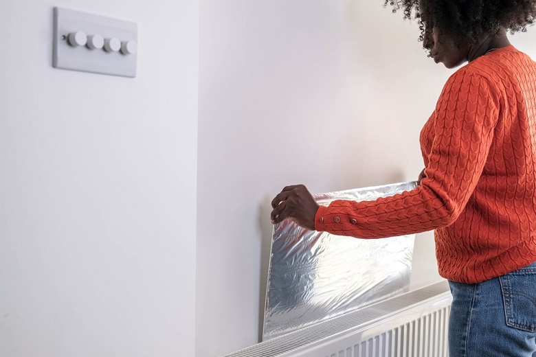A lady in an orange jumper puts reflective material behind her radiator