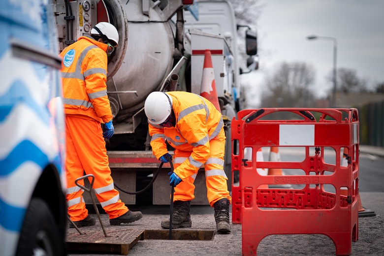 Two people in orange high-vis unblock a sewer