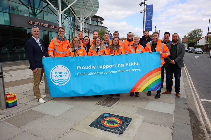 People standing behind a blue flag which reads proudly supporting pride.