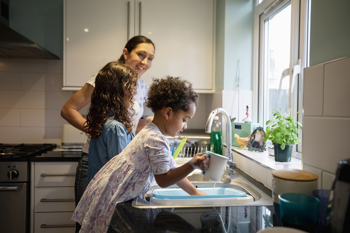 Woman does the washing up with her two children using a bowl in the sink