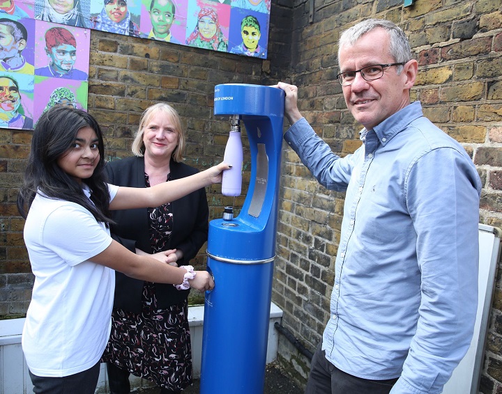 Three people using a water fountain in a school playground