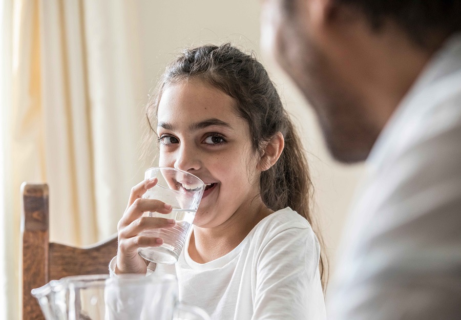 A young girl drinks a glass of water at the dining table