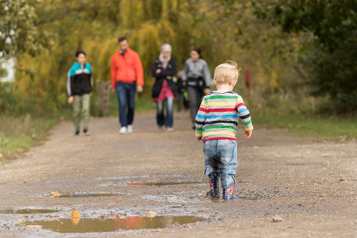 A child jumps in a puddle and a family walks in the background.