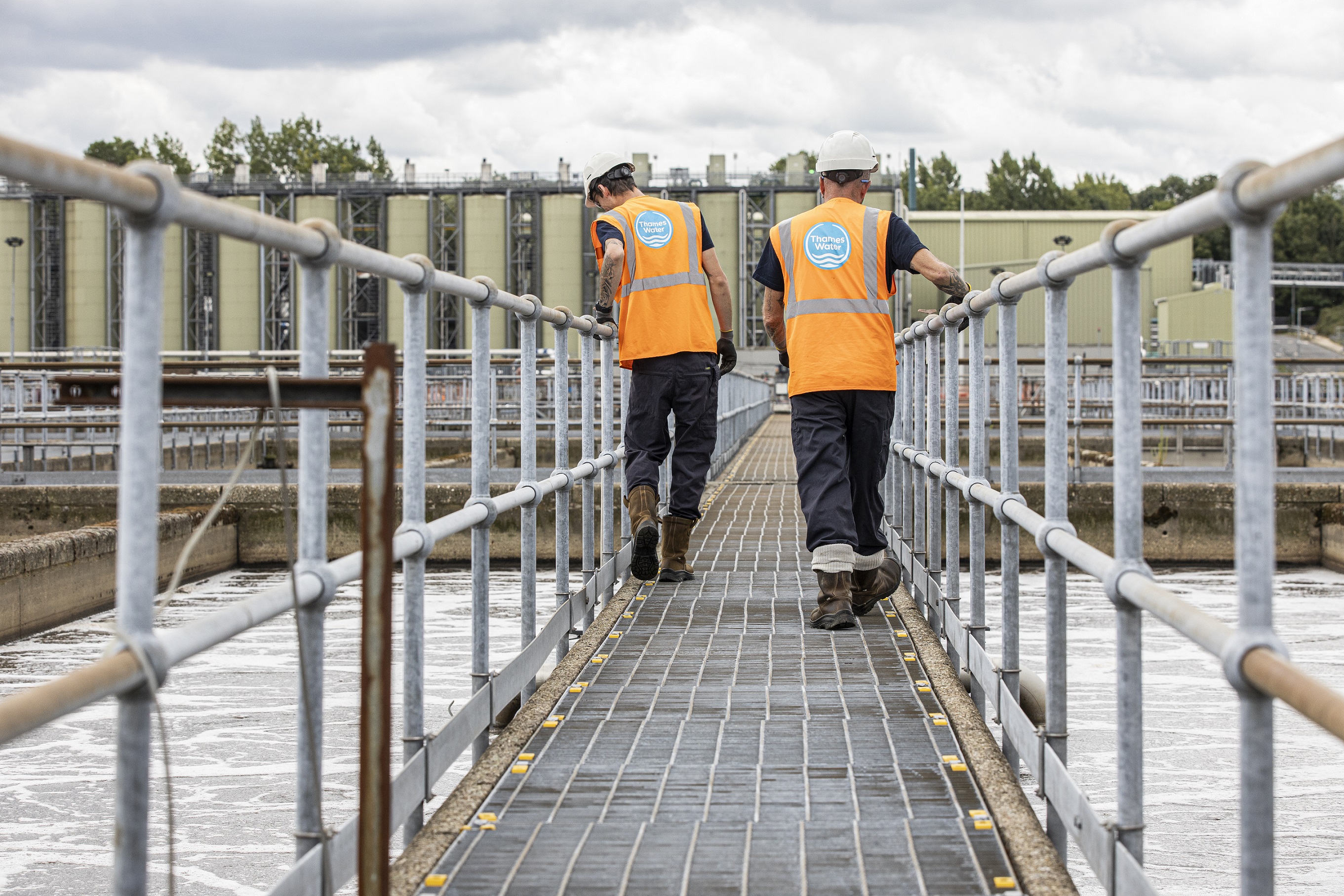 Two technicians wearing orange high-vis inspect aerations lanes at a sewage works