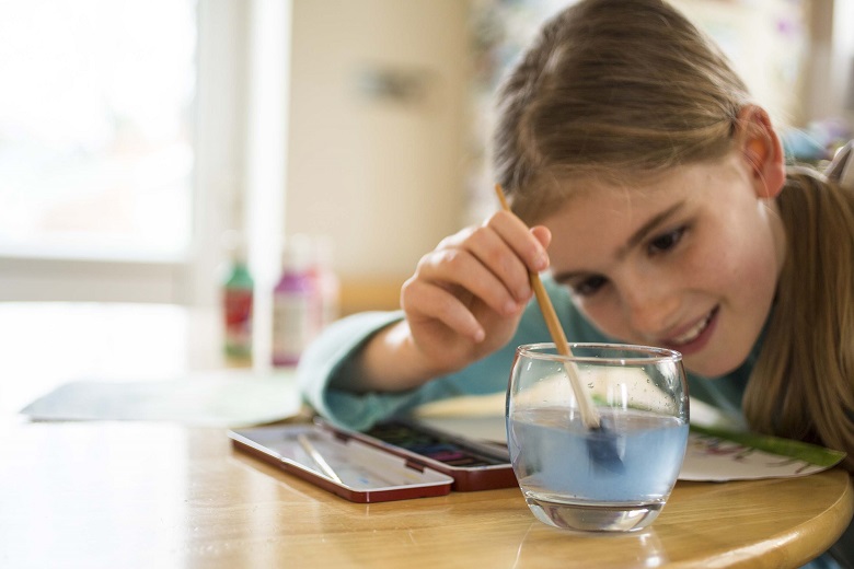 A child dipping a paintbrush in a glass of water