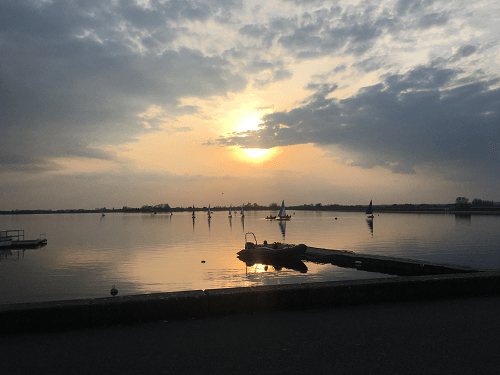 The sun setting over water with a small jetty in the middle and the bank in the foreground.