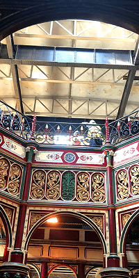 An ornate red, gold and black archway with a green floral central panel and black railings along the top.