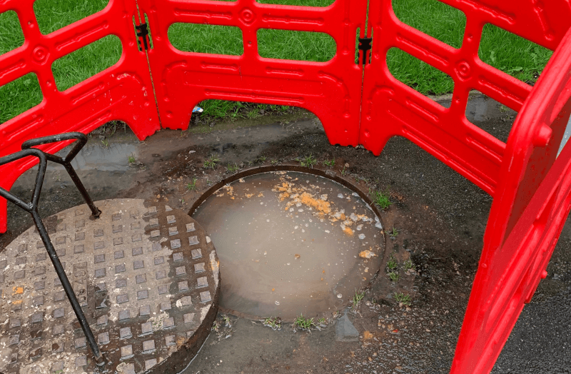 A manhole flooded by the sewer with red barrier around it
