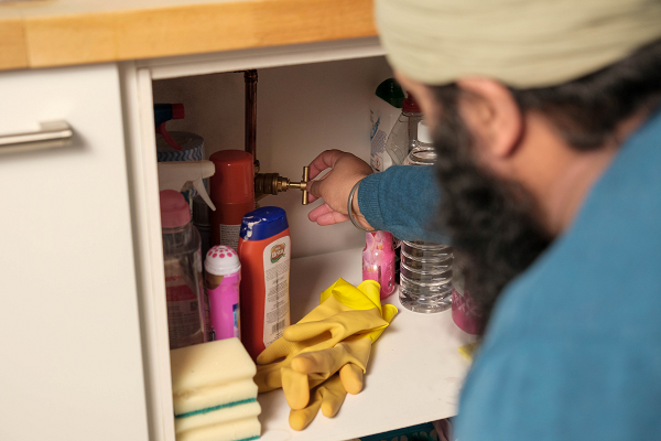 A man turning a stop valve in a kitchen cupboard
