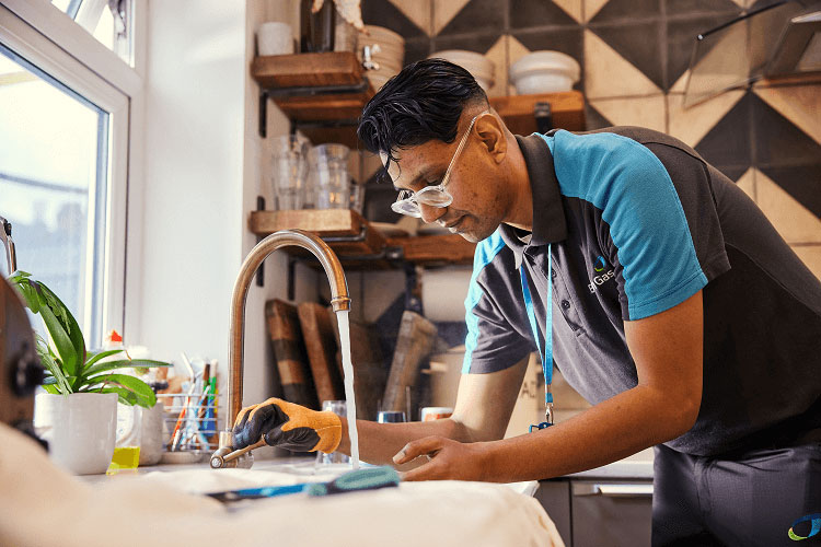 A man in a British Gas uniform working at a sink with the tap running