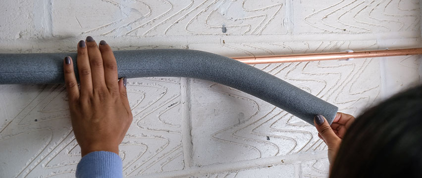 A pipe on a wall being covered with lagging