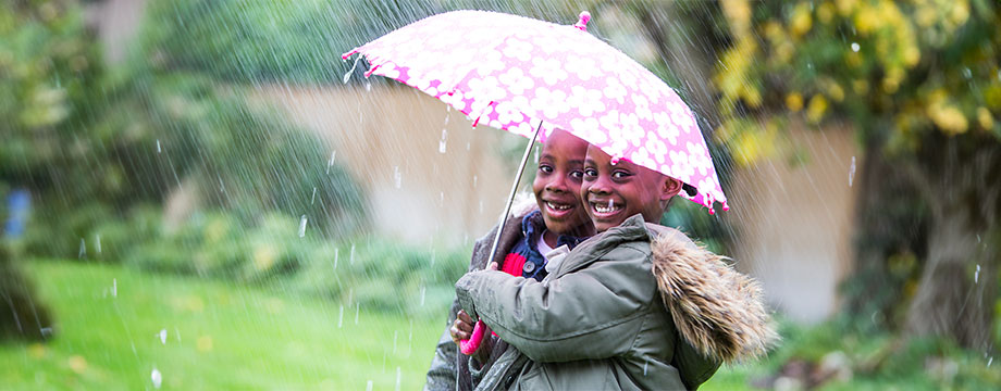 Two boys shelter from the rain under an umbrella