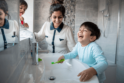 A mum helps her child to brush their teeth in the bathroom.