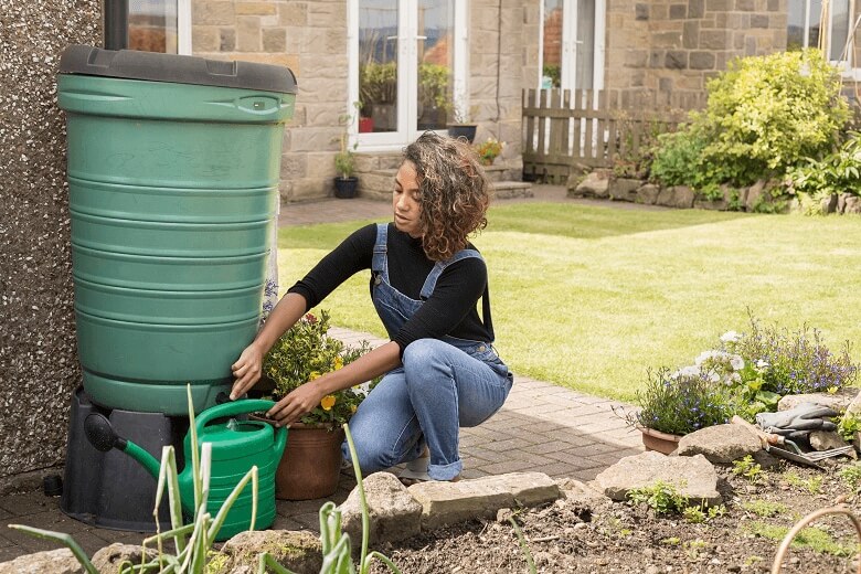 A person filling a watering can from a water butt in the garden.