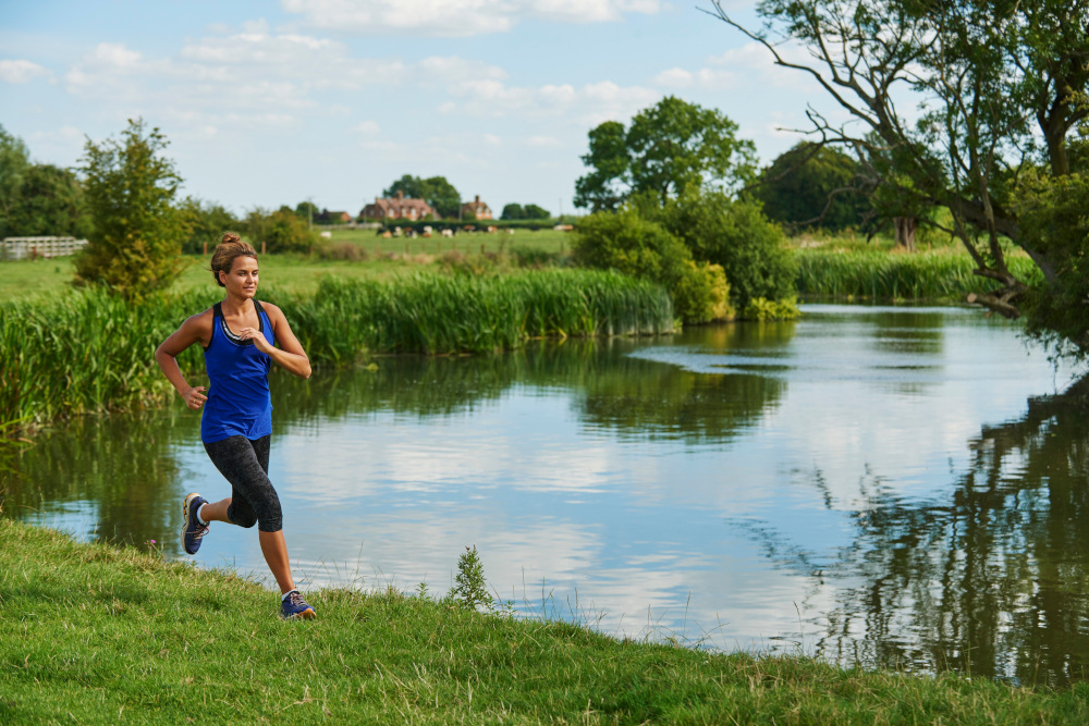 Person running along river bank on sunny day