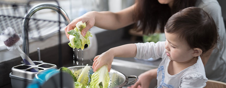 A mother and daughter wash vegetables in the sink