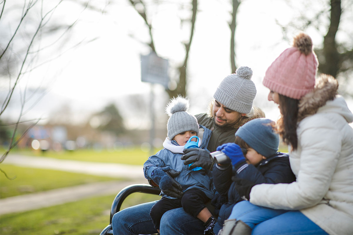 A young family on a bench in the park with winter hats on